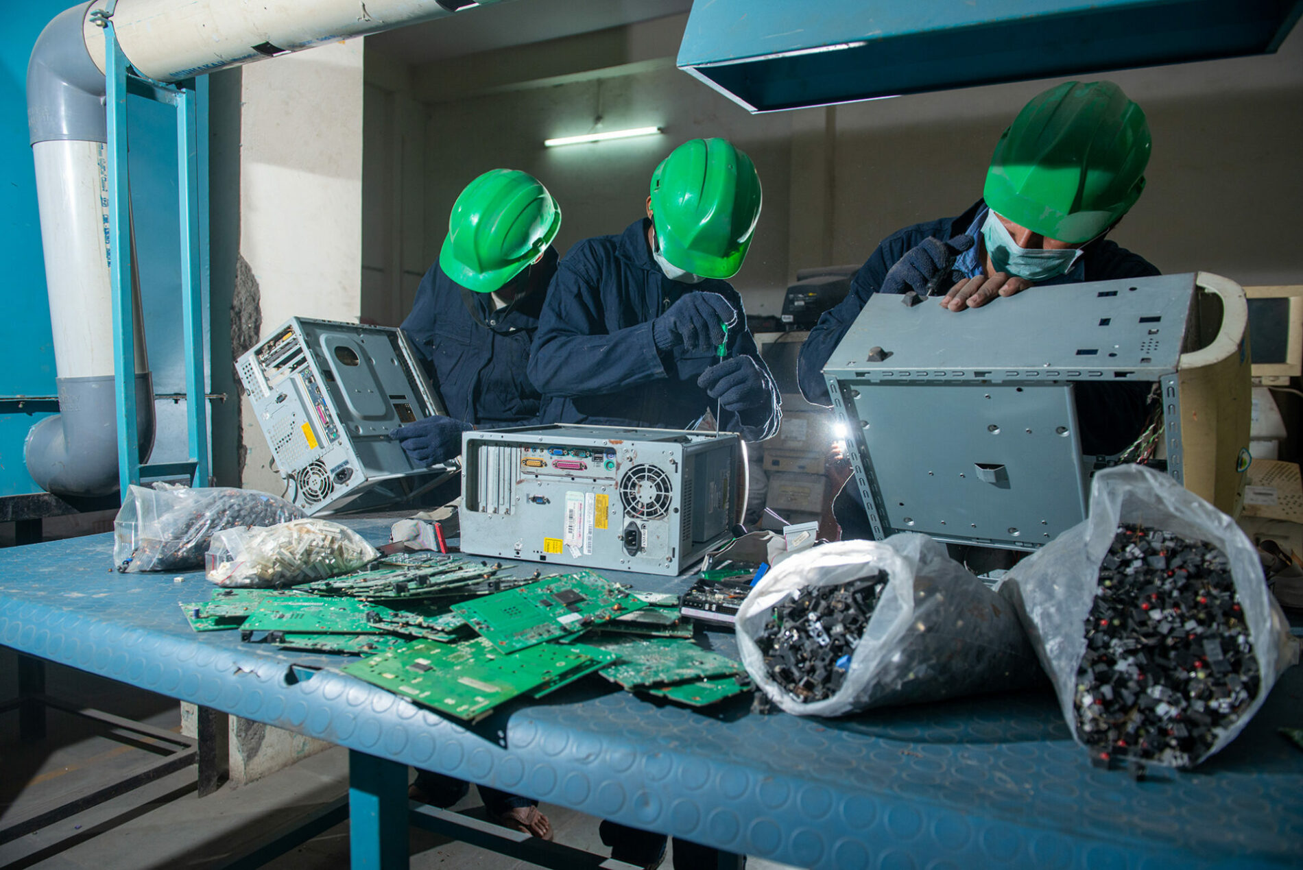 Men with green hard hats working on computer e-waste.