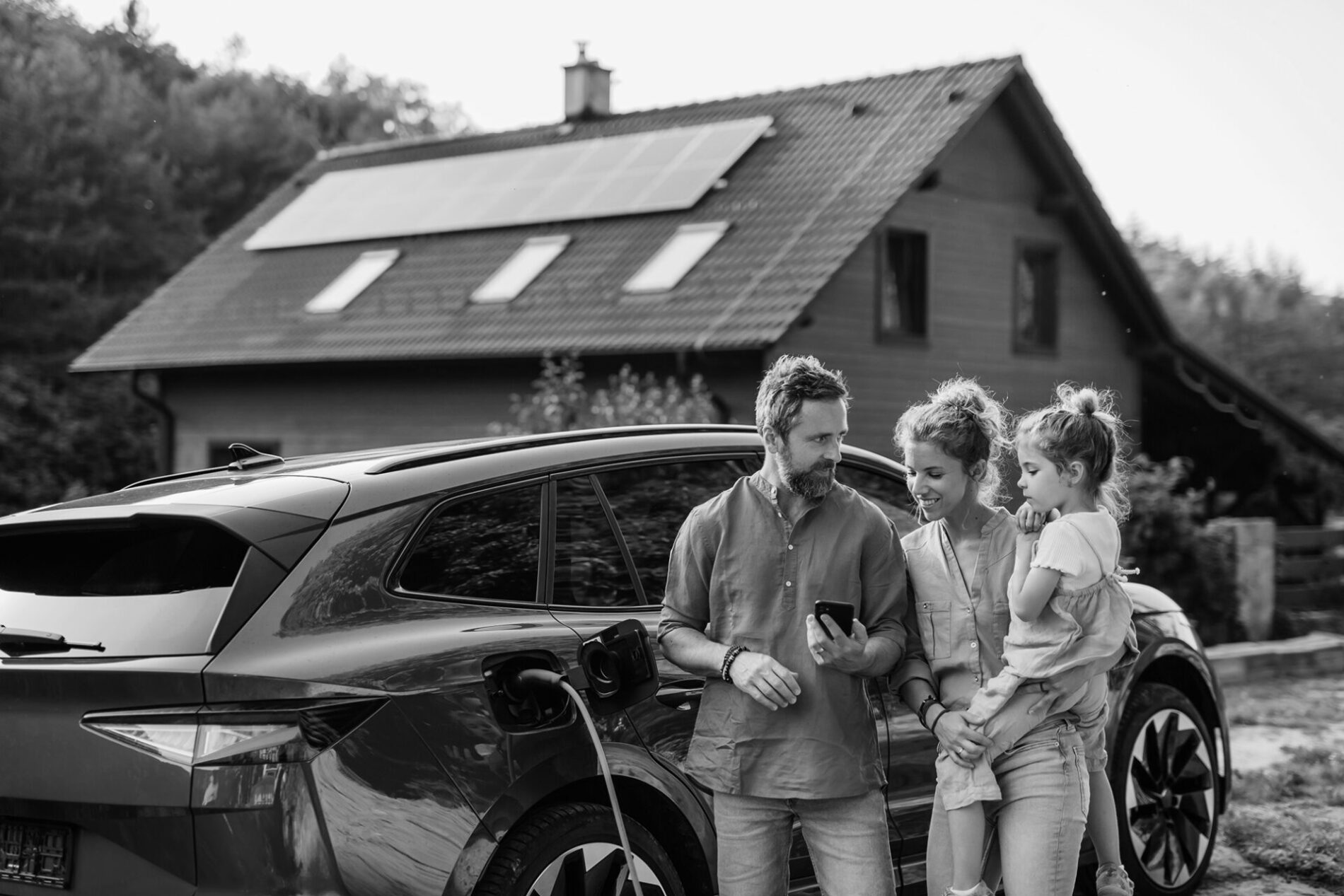 Family with little girl standing in front of their house with solar panels on the roof, having electric car.