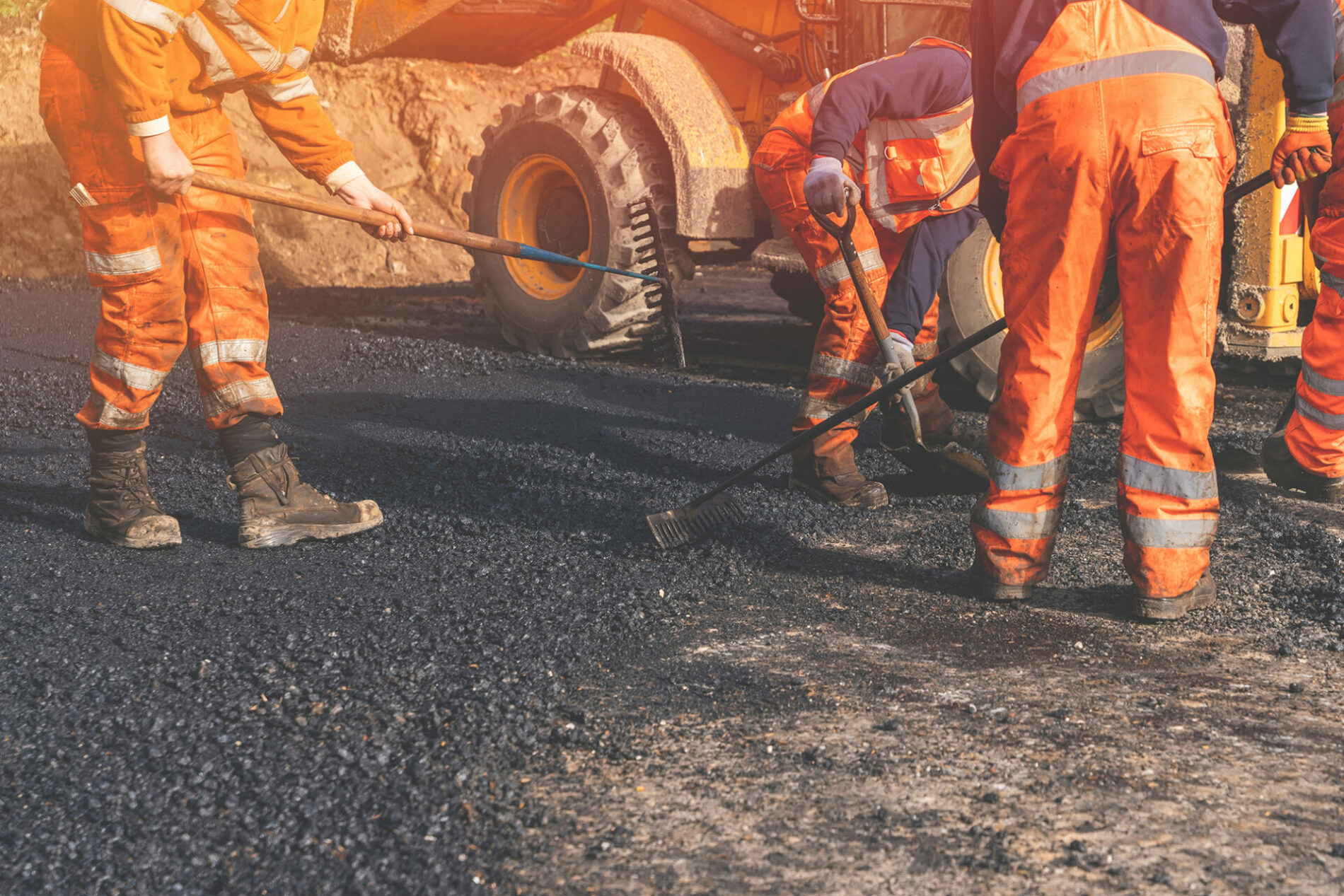 roadworkers in hi-viz and boots laying hot tarmac new road surface on residential housing development site