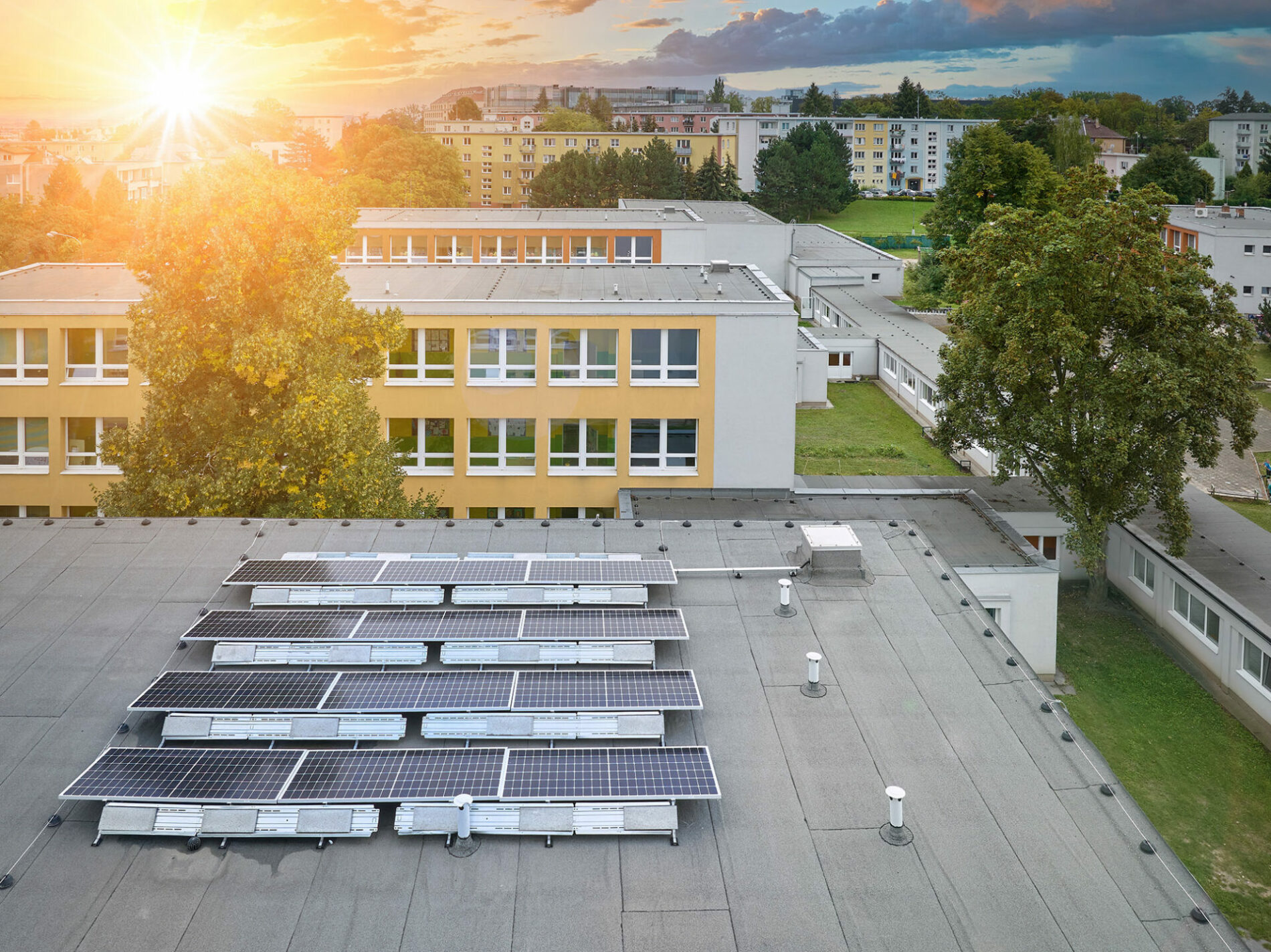 Solar power plant on the school roof. Aerial view of the photovoltaic panels against the school buildings and the city skyline, the setting sun, orange and blue.