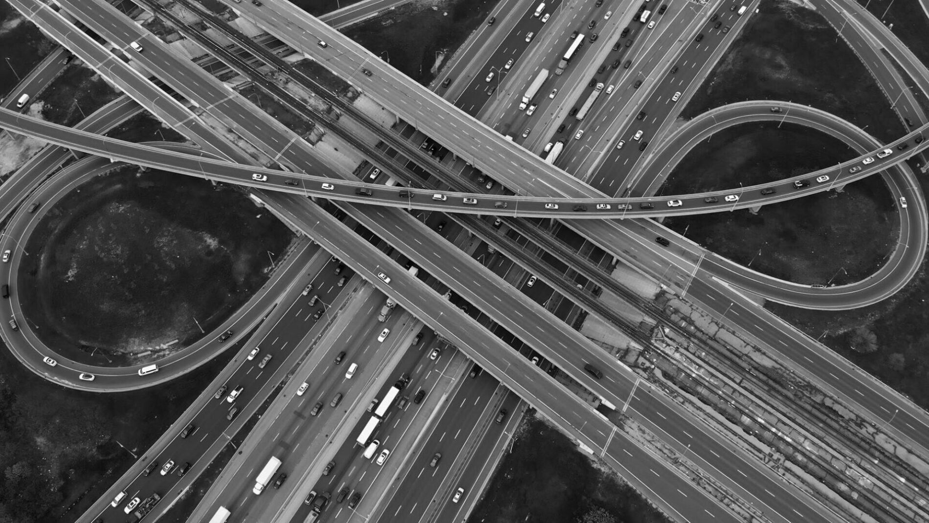 Multi-level transport interchange, busy highways interlace, seamless flow of urban traffic in motion. Sunlit highways bustle with rush hour traffic, aerial view captures city commute energy.
